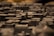 A close-up view of a detailed miniature model of a city with various buildings and structures, mostly composed of dark tones. The depth of field creates a blurred background effect, emphasizing the textured surfaces of the miniature buildings.