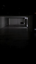 A dark, empty corridor with white walls and a gray floor. A faint light source is visible from the far end, partially illuminating the space. The sign 'C2' is displayed on one wall.