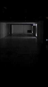 A dark, empty corridor with white walls and a gray floor. A faint light source is visible from the far end, partially illuminating the space. The sign 'C2' is displayed on one wall.