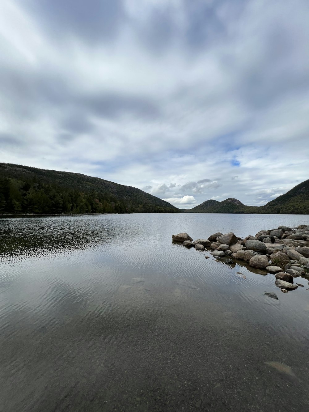 a body of water surrounded by mountains under a cloudy sky