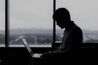 a man sitting in front of a window using a laptop computer