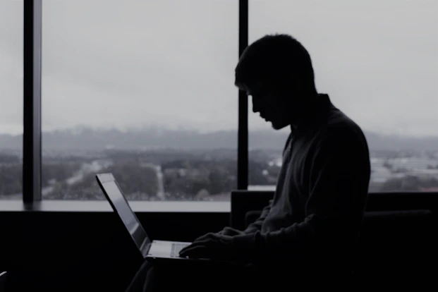 a man sitting in front of a window using a laptop computer
