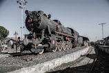 A vintage steam engine locomotive parked near a railway.