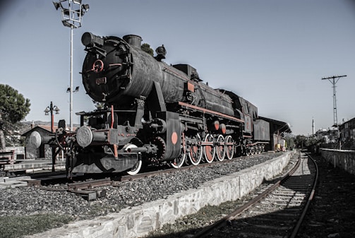 A vintage steam engine locomotive parked near a railway.