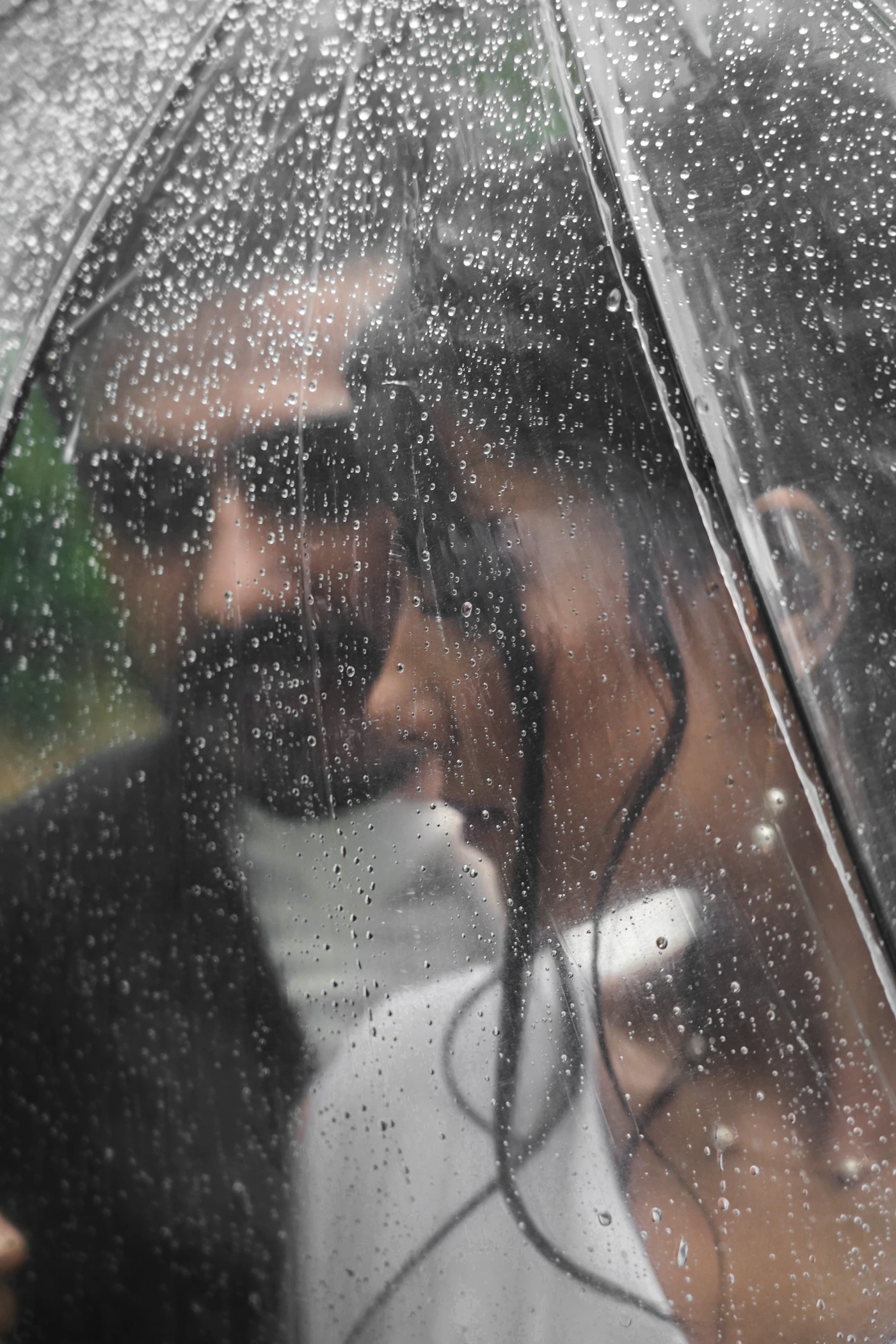A man and woman together under a clear umbrella in the rain showing the specific wedding photograph that only wet conditions can produce