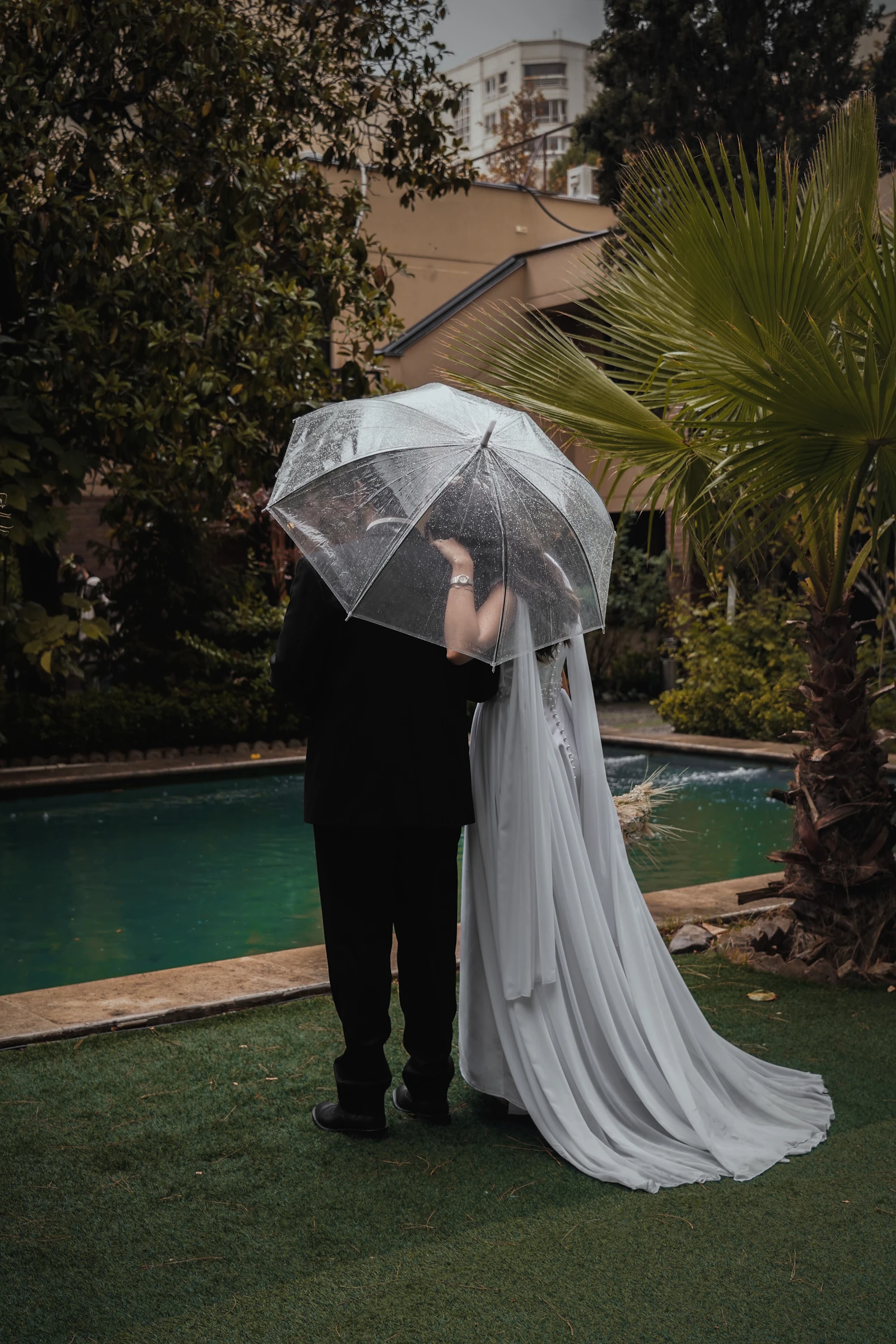 A bride and groom standing close together under a large umbrella in the rain