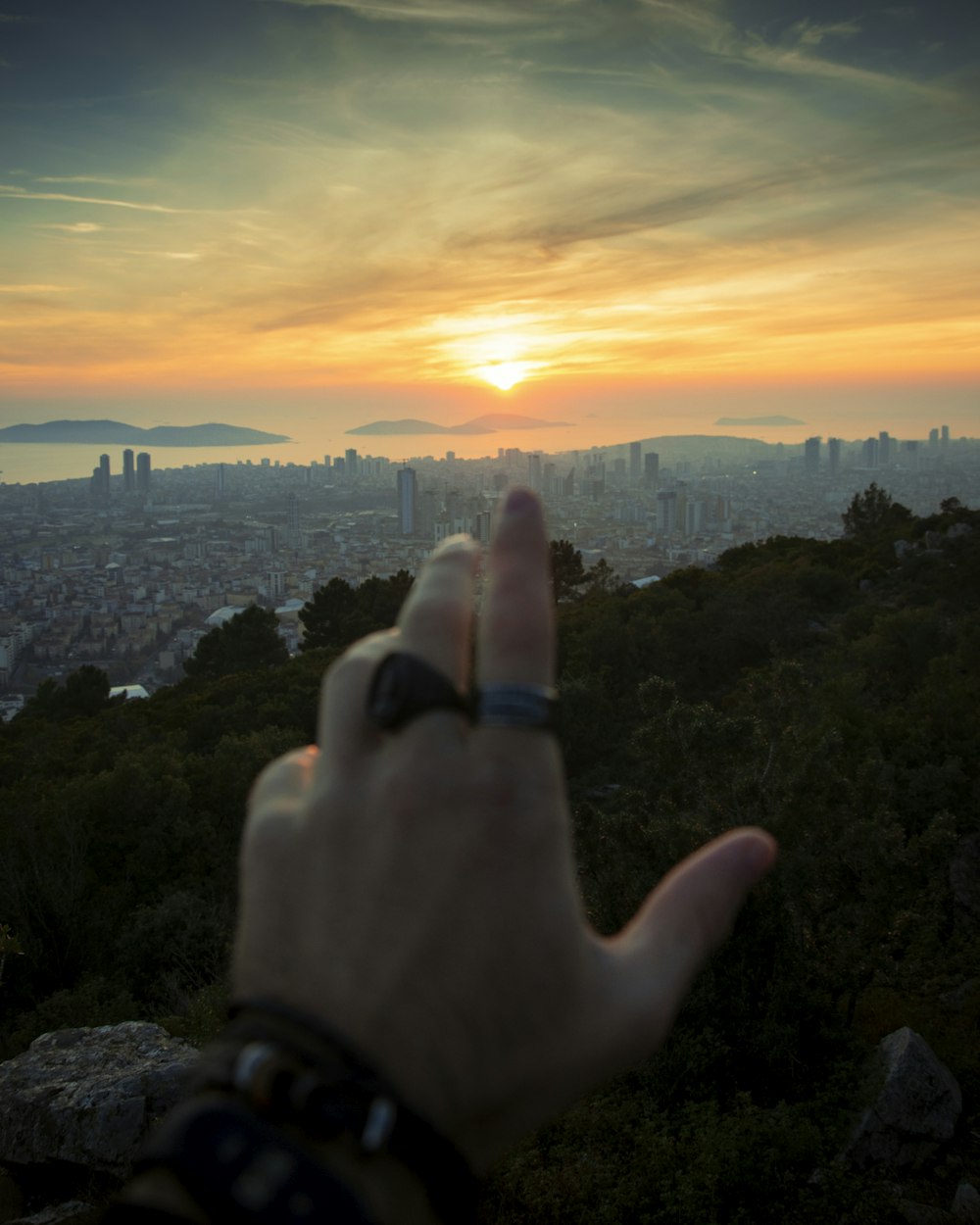 a hand pointing at the sunset over a city