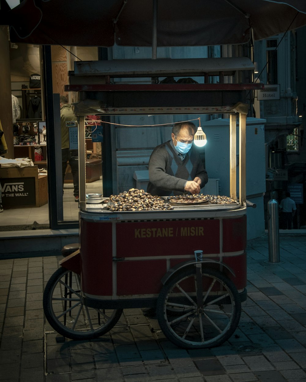 a man wearing a face mask behind a food cart