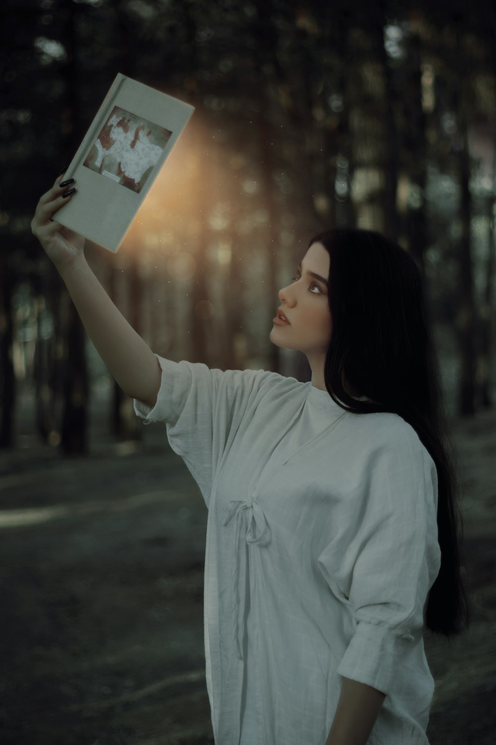 a woman holding up a book in a forest