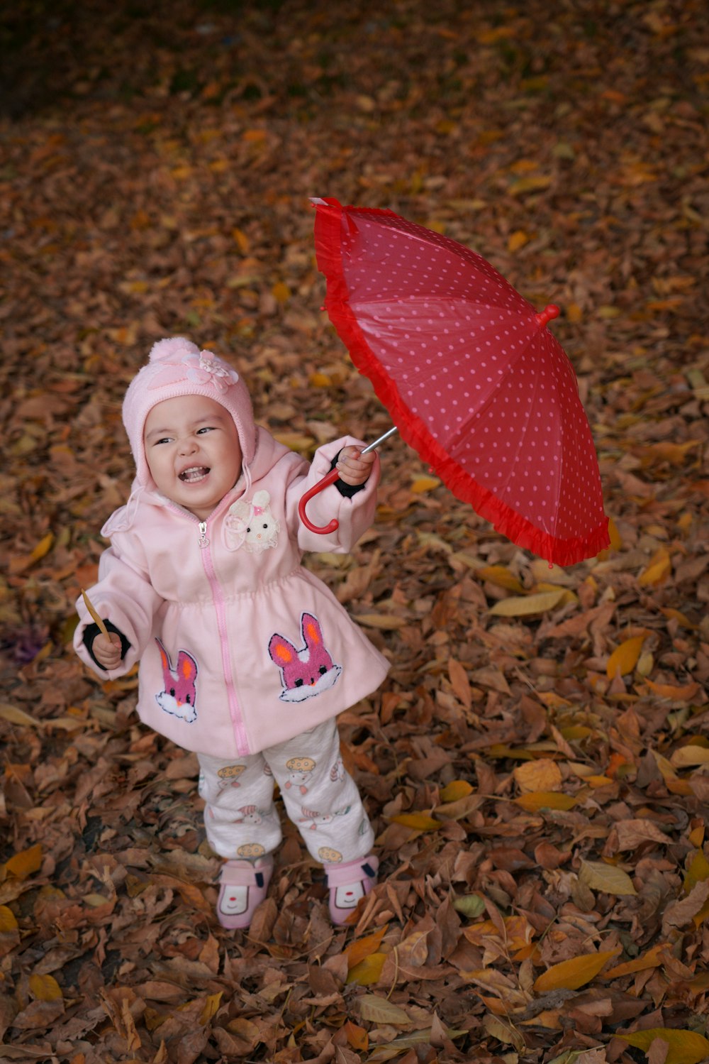 a little girl in a pink coat holding a red umbrella