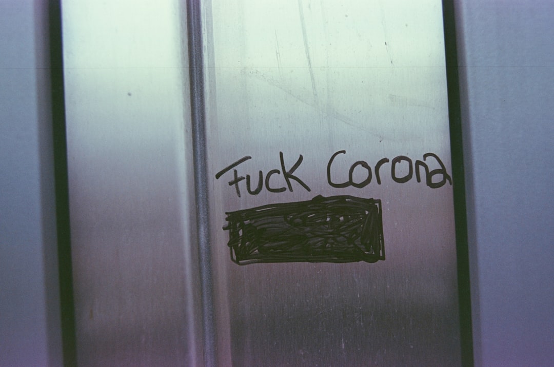 a close up of a metal door with writing on it, FUCK CORONA. Leica R7 (1994), Summicron-R 2.0 35mm (1978). Hi-Res analog scan by www.totallyinfocus.com – Kodak Elite Chrome 100 (expired 2001)<p></figure>