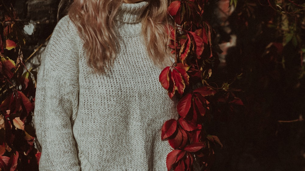 a woman standing in front of a tree with red leaves