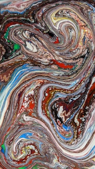 A vibrant abstract painting featuring swirling patterns of paint. The design is composed of intricate swirls and lines in a mix of colors, including deep reds, earthy browns, bright blues, and hints of green and yellow. The paint appears to be in motion, creating a dynamic and fluid composition.