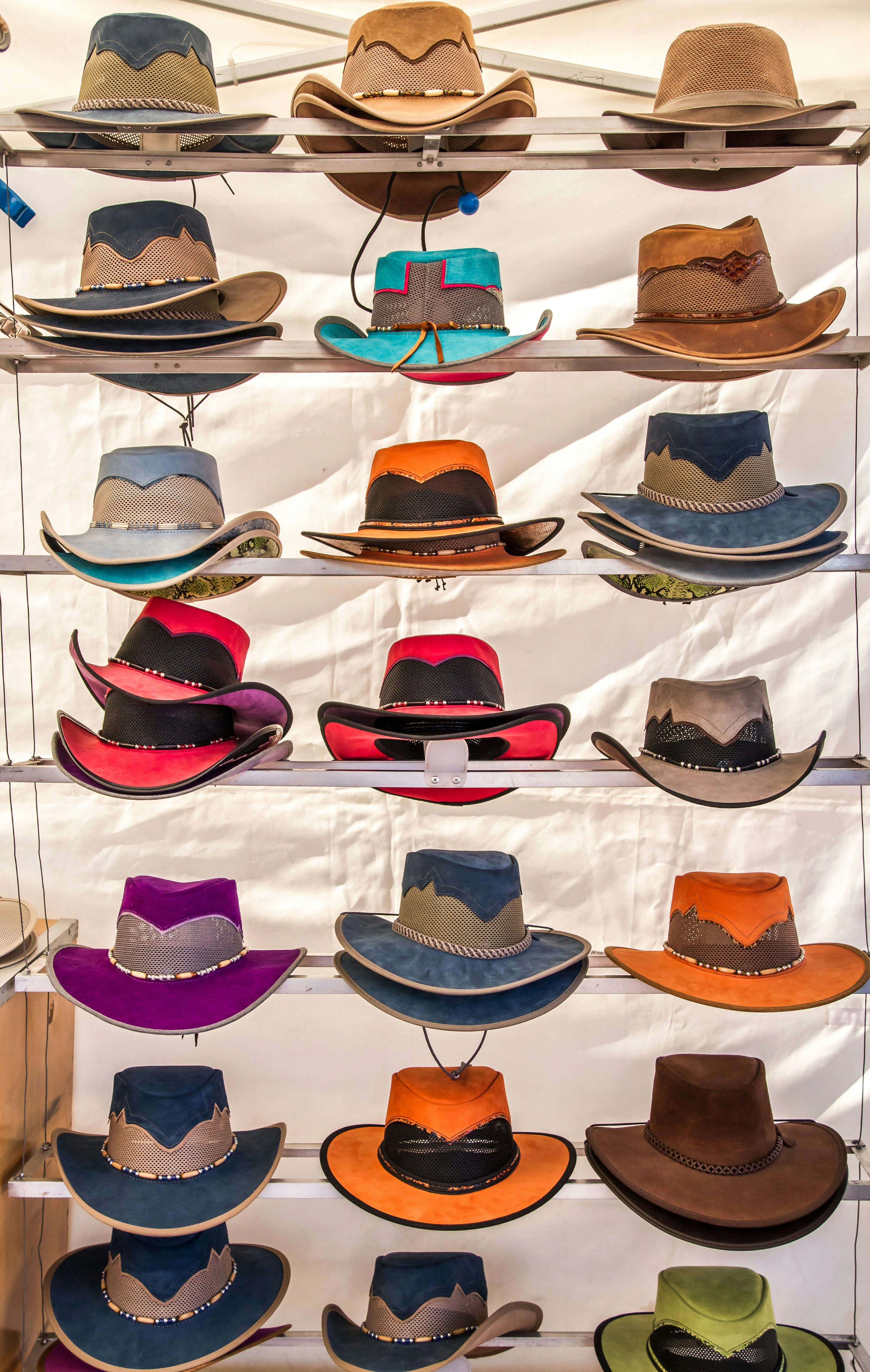 Multiple cowboy hats of various colors and styles are neatly arranged on shelves, each featuring unique designs and details including different textures and band patterns.