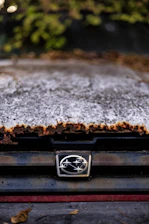 Close-up of a classic rust bucket car’s weathered hood ornament with a subtle cross in the background.