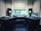 A music production studio setup featuring two computer monitors displaying a digital audio workstation, a laptop with an animated image on the screen, two studio speakers on stands, a MIDI keyboard, and other audio equipment on a curved desk.
