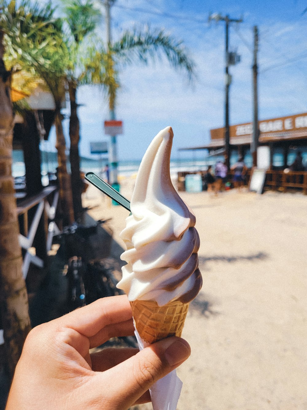 a hand holding an ice cream cone on a beach