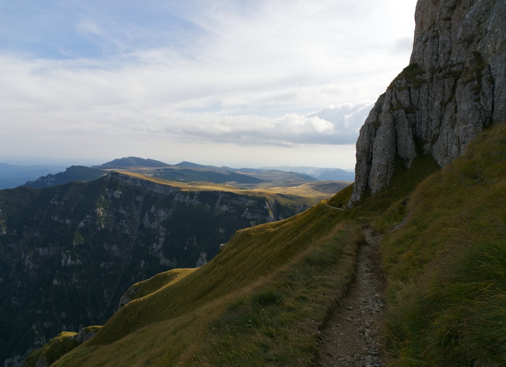 a path going up a grassy hill with mountains in the background