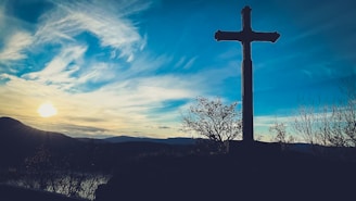 A distant mountain with a cross silhouetted against a colorful sunset sky.