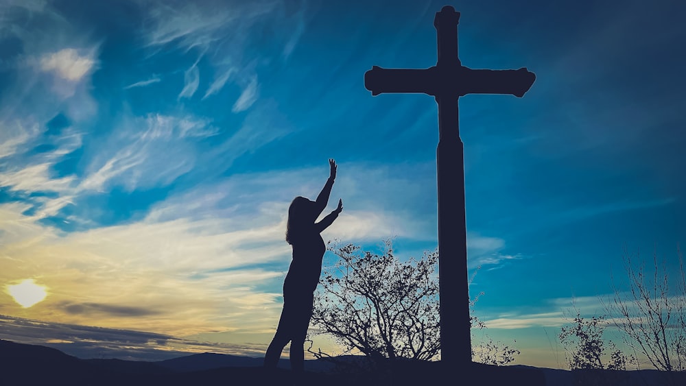 a silhouette of a person reaching up to a cross