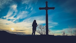 a person standing in front of a cross at sunset