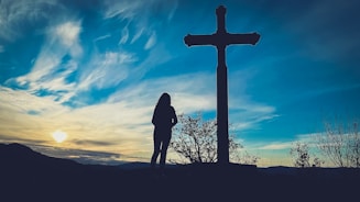a person standing in front of a cross at sunset