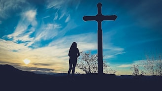 a person standing in front of a cross at sunset