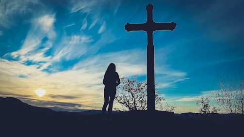 a person standing in front of a cross at sunset