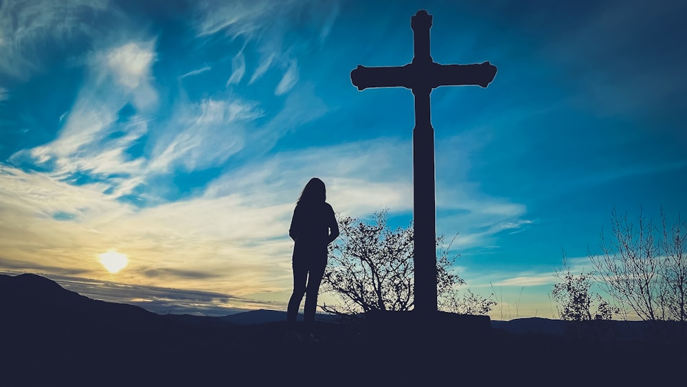 una persona in piedi davanti a una croce al tramonto