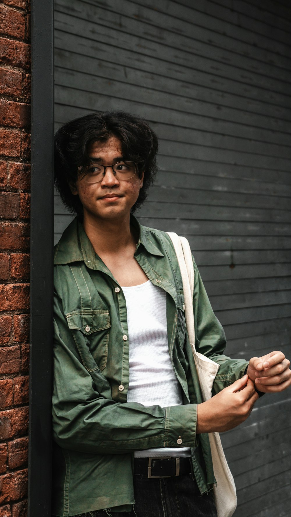 a man with glasses leaning against a brick wall