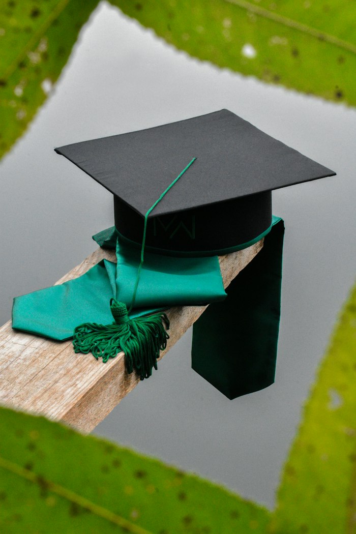 Black graduation cap with a green tassel on a wooden beam