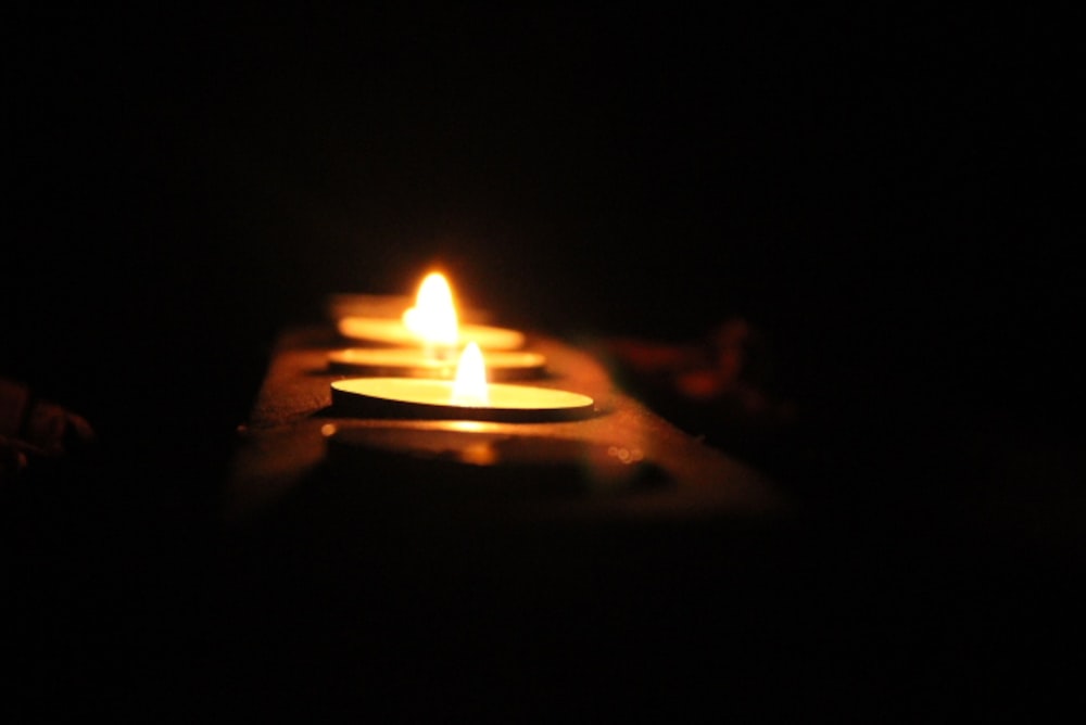 three lit candles sitting on a table in the dark