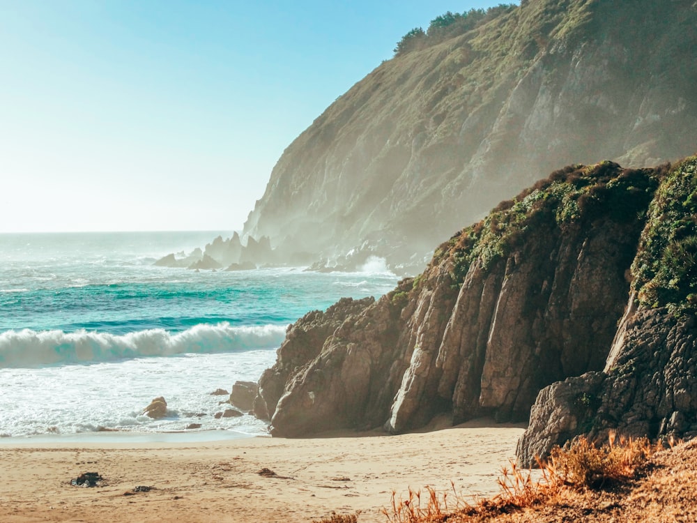 a sandy beach next to the ocean with a cliff in the background