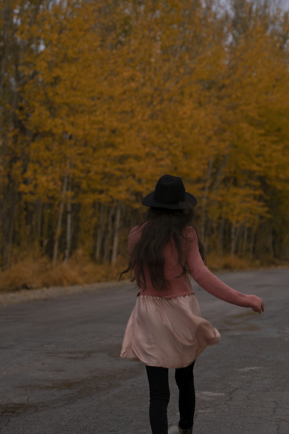 ドレスと帽子をかぶった女の子が道をスケートボードで下る