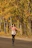 A joyful woman walking along a leafy park path in autumn, leaves swirling around her.