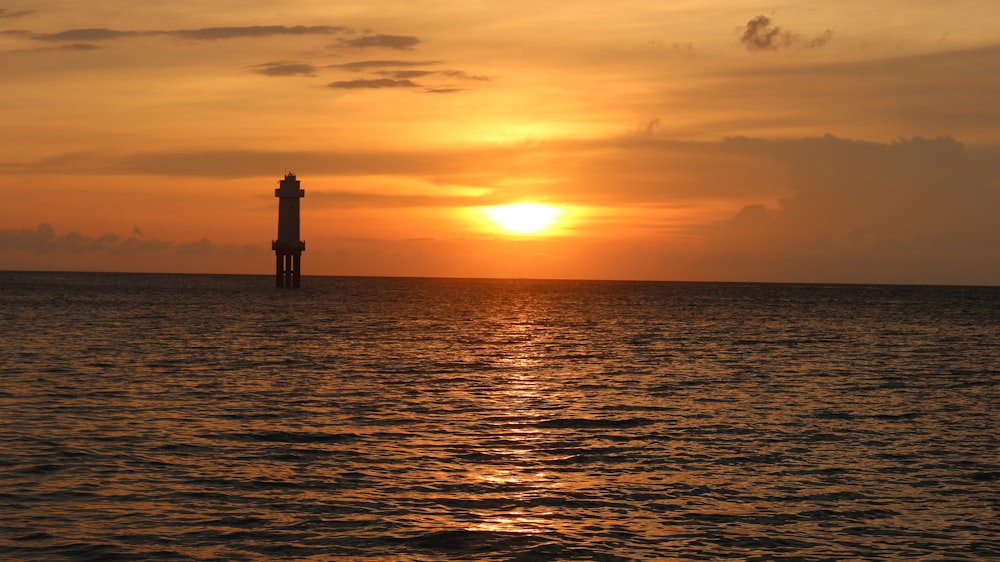 the sun is setting over the ocean with a lighthouse in the distance