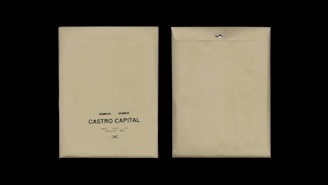 Two beige envelopes are displayed against a black background. The envelope on the left has printed text reading 'Desarrollo I, Rie, Auto Marketing, Castro Capital' with a decorative symbol below. The envelope on the right is flipped to show the plain back with a metal clasp.