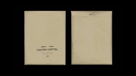 Two beige envelopes are displayed against a black background. The envelope on the left has printed text reading 'Desarrollo I, Rie, Auto Marketing, Castro Capital' with a decorative symbol below. The envelope on the right is flipped to show the plain back with a metal clasp.