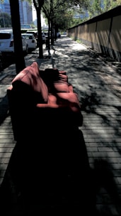 A friendly mover carefully carrying a couch down a sunny neighborhood street.