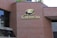 A brick building façade features a sign with the text 'Ville de Gatineau' accompanied by a logo. The sign is mounted on the building's wall, which is composed of red bricks. There are window reflections visible on the left side of the image.
