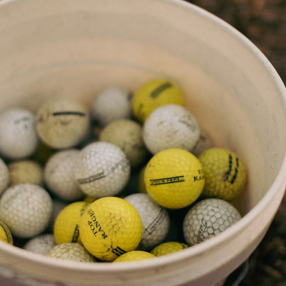 Un cubo lleno de pelotas de golf amarillas y blancas