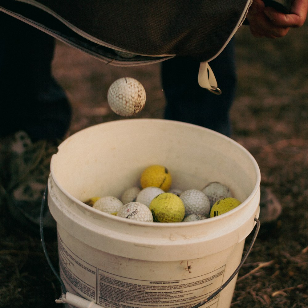 a bucket full of golf balls with a person standing next to it