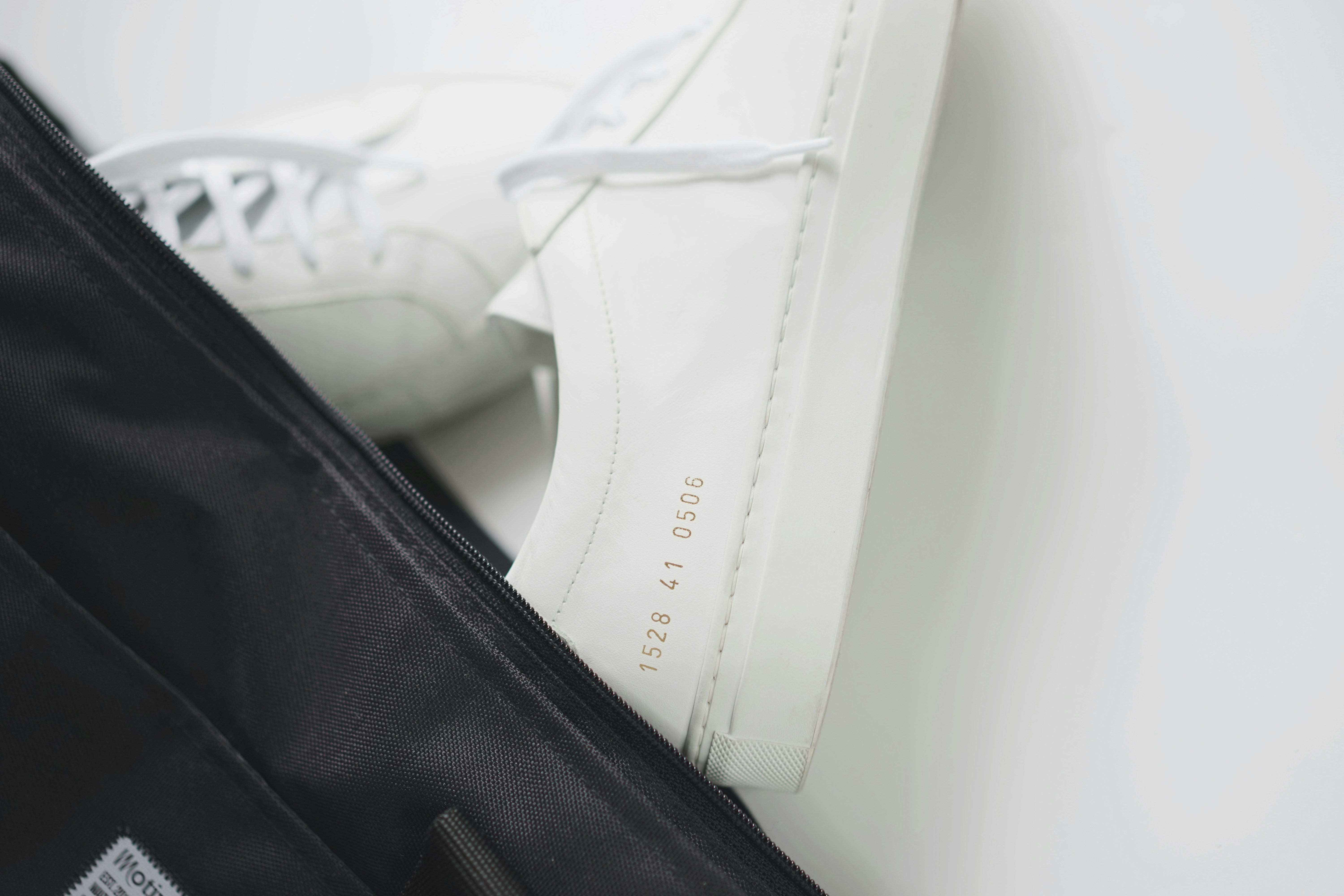 a pair of white shoes sitting on top of a black bag
