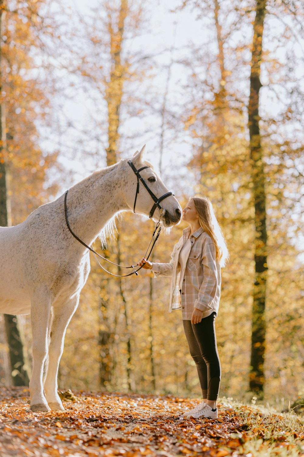 a woman standing next to a white horse in a forest