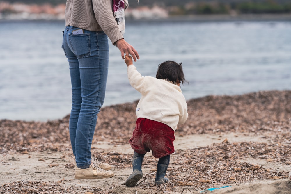 a woman holding the hand of a child on a beach
