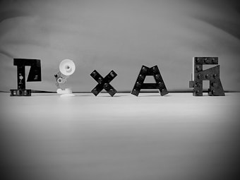 Lego blocks are arranged to spell out a word, accompanied by a small construction resembling a desk lamp. The background is plain, enhancing focus on the objects.