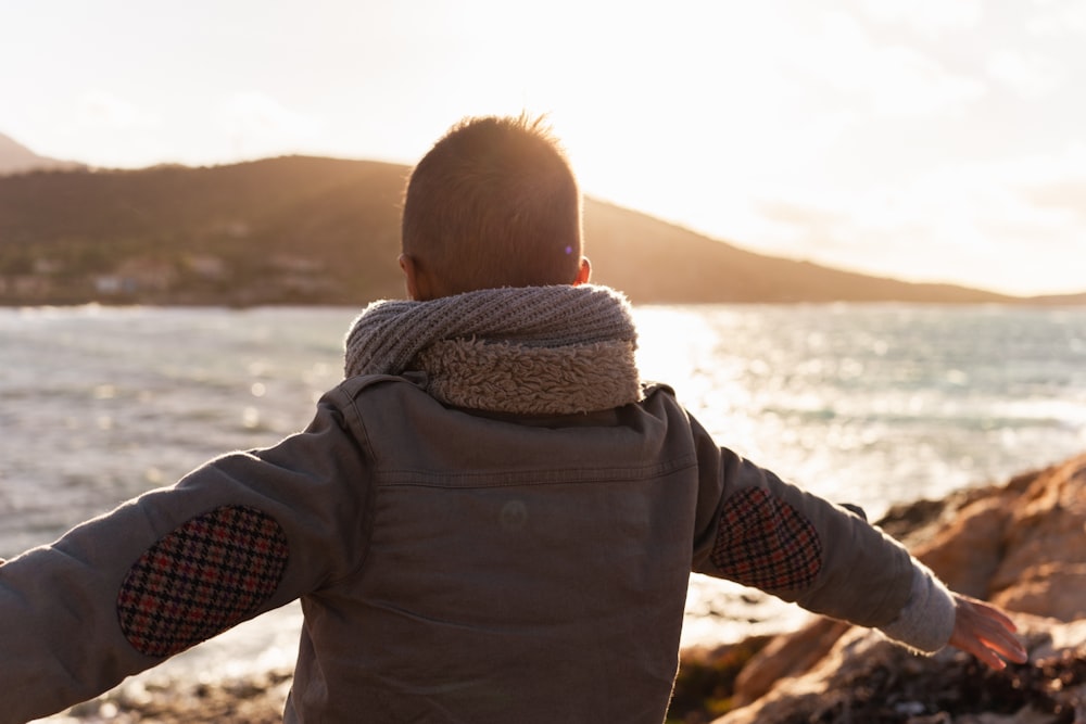 a young boy standing on a beach next to the ocean