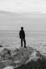 a man standing on top of a rock next to the ocean