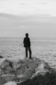 a man standing on top of a rock next to the ocean