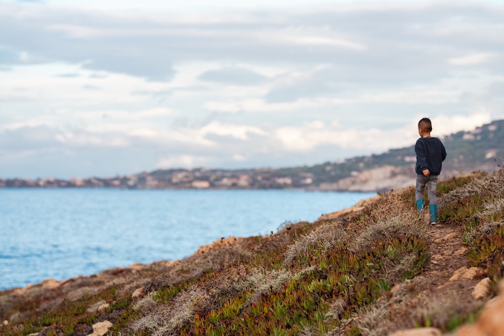 a young boy walking up a hill next to a body of water